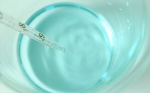 A thermometer measuring the temperature of a clear blue liquid in a glass container.