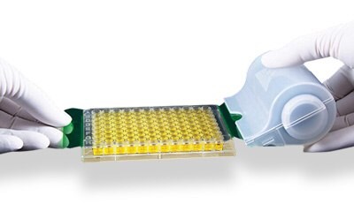 Photograph showing two gloved hands using an adhesive seal on a roller to seal a microplate.