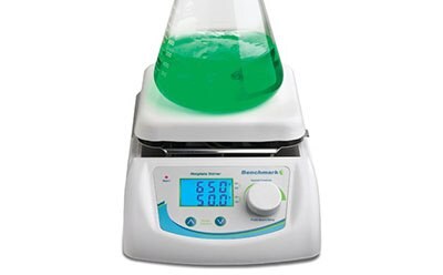 A digital magnetic hotplate stirrer with a green liquid in a glass beaker placed on top, displaying temperature and speed settings on its screen, with the brand name ‘Heidolph’ and model ‘Hei-Mix L’ visible.