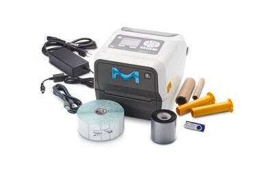 Portable, compact label printer with a white and grey body featuring a blue “M” logo on the front. Accompanying the printer are various accessories, including a power adapter with cables, three cylindrical objects resembling ink rolls in yellow and black colors, a small blue plastic piece that appears to be part of the printer mechanism, and a roll of labels. 