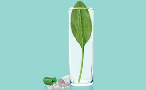 The image depicts a clear glass of water containing a single green leaf, surrounded by scattered pills and capsules. One of the capsules is open, revealing its powder contents.