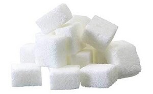 The image depicts a pile of uniformly shaped, bright white sugar cubes against a white background, with their edges slightly blending into the background.