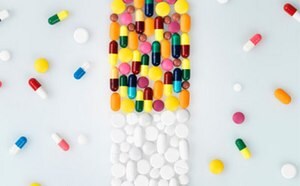 The image depicts an array of colorful pills and capsules artistically arranged on a white surface to resemble the shape of a pill bottle, with the body composed of multi-colored capsules and the cap made of white round tablets, surrounded by additional loose pills.