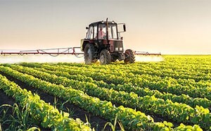 A tractor with extended arms is tending to a vibrant green crop field under a clear sky, symbolizing productive agricultural activity in a serene rural setting.