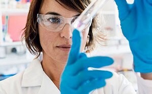 A scientist or lab technician in a white coat and blue gloves is engaged in an experiment or analysis in a laboratory setting.