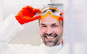 Male scientist with orange safety goggles and red gloves removing his goggles