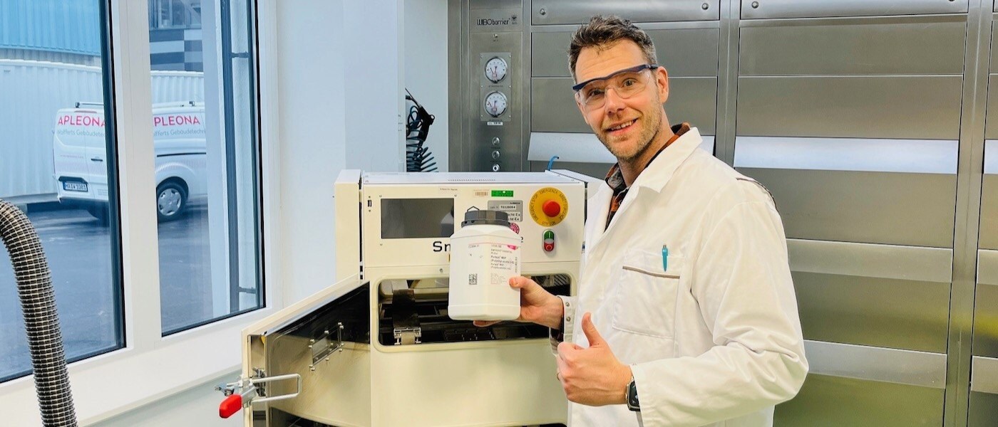 Thomas Kipping in lab Thomas Kipping이 보안경과 실험복을 착용하고 레이저 3D 프린터 옆에 서 있습니다.