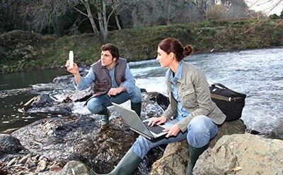 Two scientists testing the water at a river.